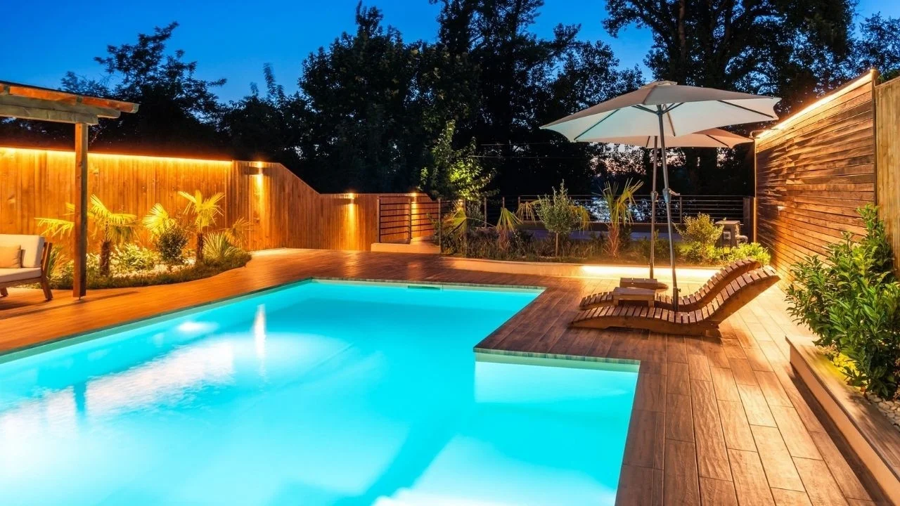 Resort-style swimming pool illuminated at night with lounge chairs